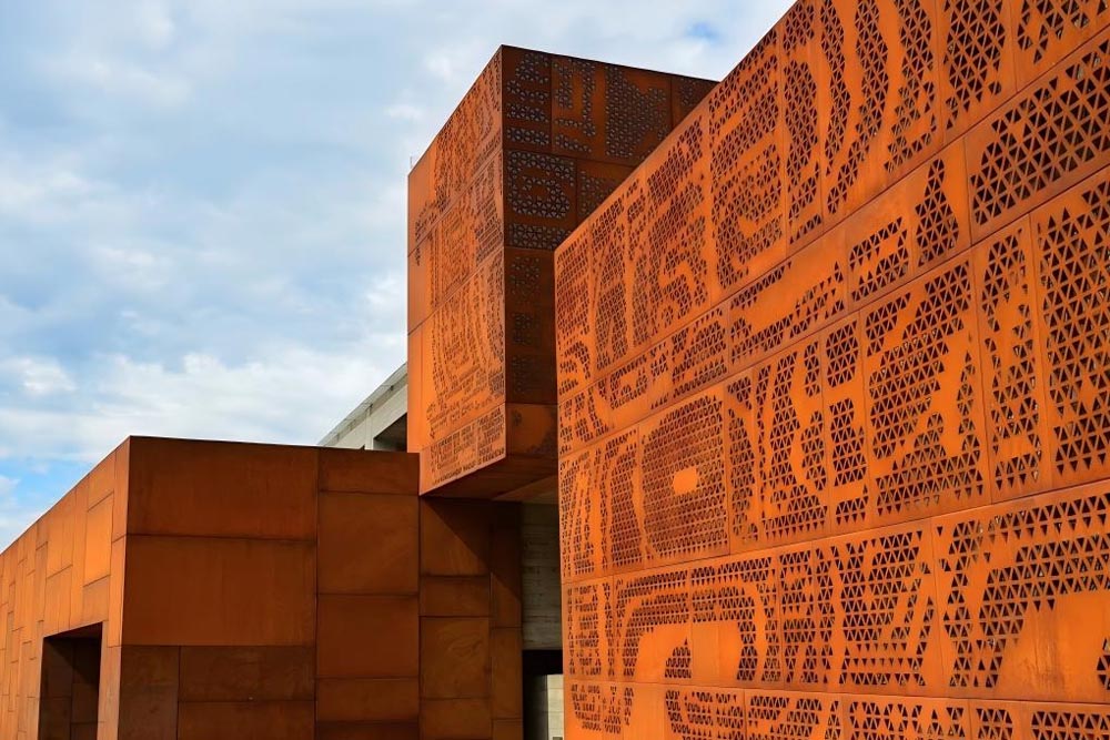 Perforated corten steel facade panels on a modern architectural building exterior with warm rust-toned metal surface and precision-cut geometric perforations.